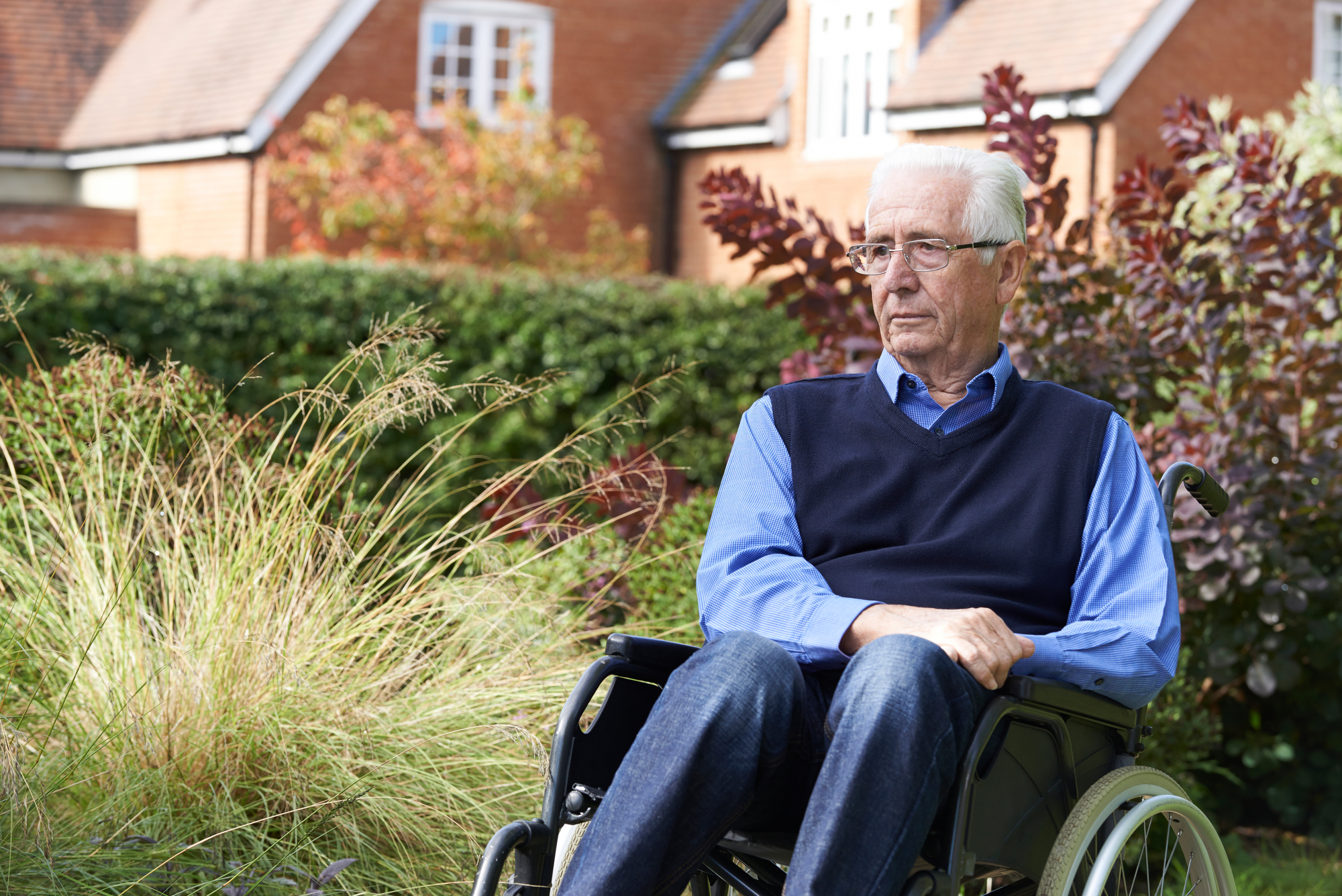 A depressed senior man sitting outdoors in a wheelchair, symbolizing the issue of nursing home neglect